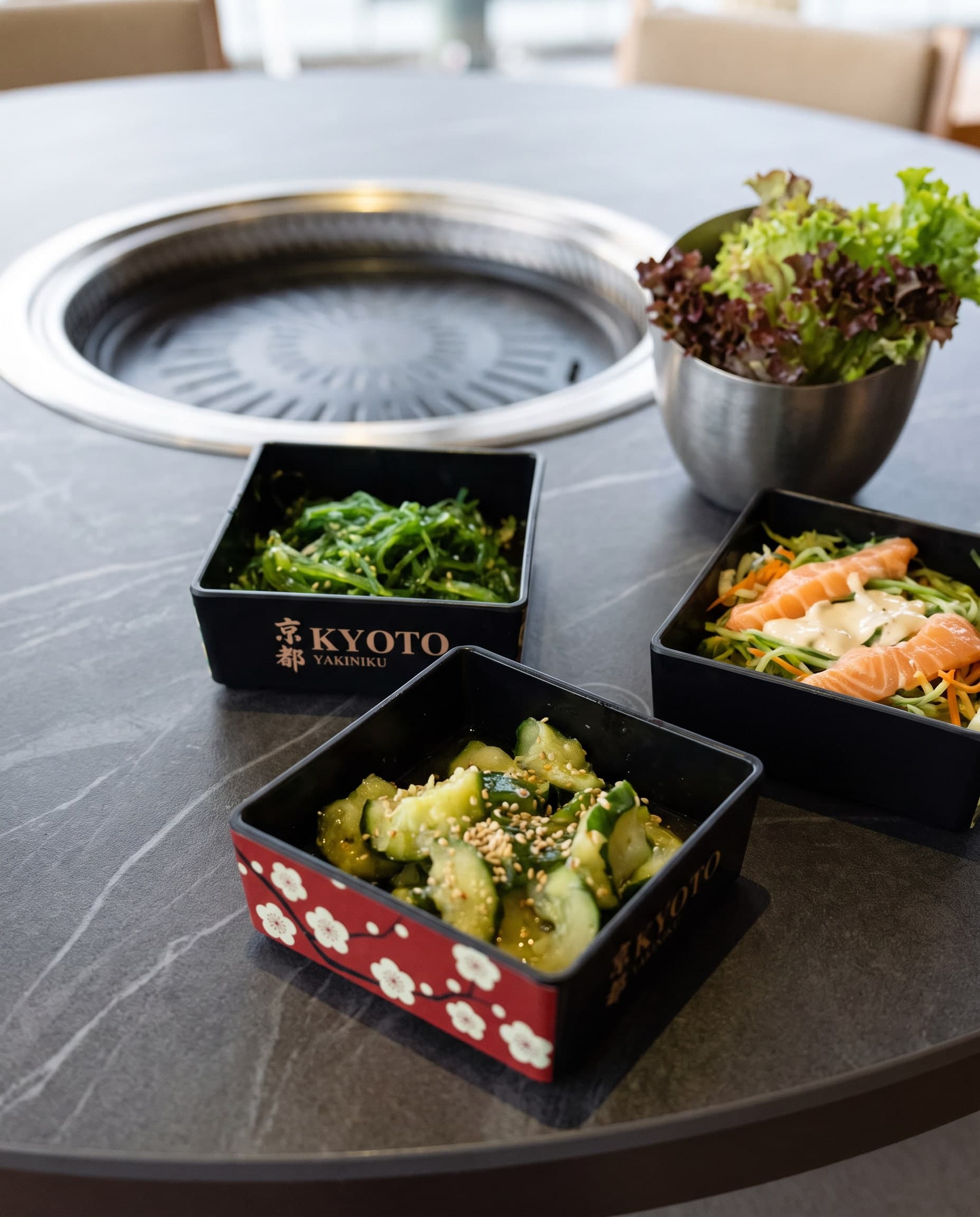 Gurkensalat mit Sesam, Wakame-Salat und Salat mit Lachs in Boxen, dahinter frischer Blattsalat